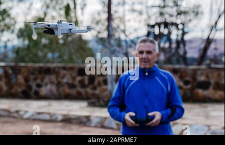 Vorderansicht des alten Mannes, der während des Stehens gegen Bäume im Park Drohne fliegt, Fokus auf die Drohne Stockfoto