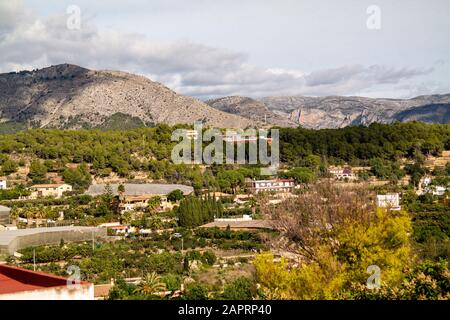 Vogelperspektive auf üppige Natur und Gebäude von Polop Stadt in Spanien mit Bergen im Hintergrund Stockfoto