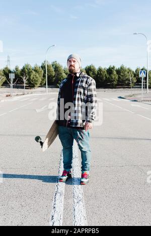 Porträt eines modernen Mannes, der das Longboard hält. Skateboarding-Konzept. Stockfoto