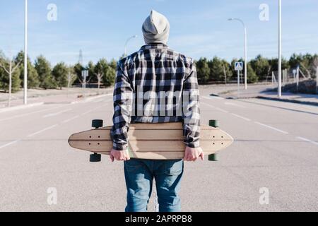 Nahaufnahme eines Mannes auf dem Rücken, der das Langbrett hält. Skateboarding-Konzept. Stockfoto