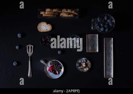 Luftaufnahme von Beeren und Brot in kleinen Behältern mit Schwarze Farbe im Hintergrund Stockfoto