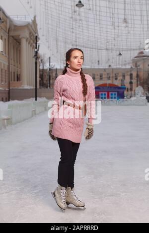 Junge hübsche Frau bekleidet rosafarbenes Sweatshirt, das in Schlittschuhbahnen, Eisbahn im Freien, auf Eis steht Stockfoto