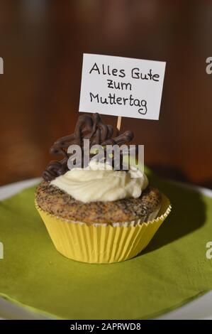 Cupcake mit einem Hinweisschild: Alles GUTE ZUM MUTTERTAG auf Deutsch, was GLÜCKLICHEN MUTTERTAG auf einem Teller bedeutet Stockfoto
