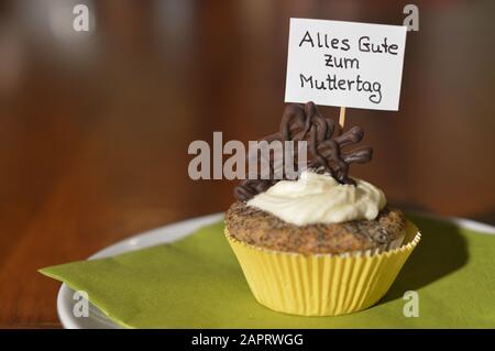 Cupcake mit einem Hinweisschild: Alles GUTE ZUM MUTTERTAG auf Deutsch, was GLÜCKLICHEN MUTTERTAG auf einem Teller bedeutet Stockfoto