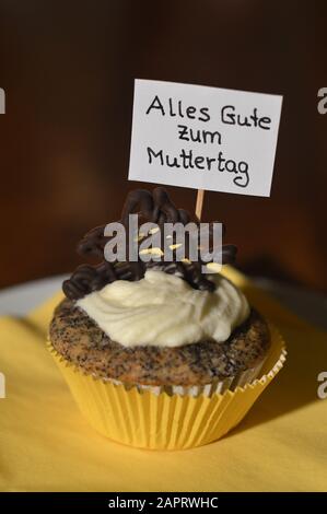 Cupcake mit einem Hinweisschild: Alles GUTE ZUM MUTTERTAG auf Deutsch, was GLÜCKLICHEN MUTTERTAG auf einem Teller bedeutet Stockfoto