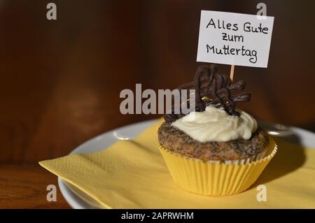 Cupcake mit einem Hinweisschild: Alles GUTE ZUM MUTTERTAG auf Deutsch, was GLÜCKLICHEN MUTTERTAG auf einem Teller bedeutet Stockfoto
