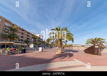 Strandpromenade in Puerto de Mazarron, Murcia, Costa Calida, Spanien, an der Mittelmeerküste. Leute in der Bar im Freien, Café. Fischerskulptur Stockfoto