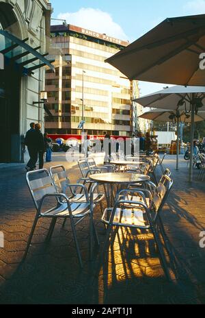 Spanien. Barcelona. Leere Stühle im Straßencafé und Blick auf das Gebäude des Banco Pastor. Stockfoto