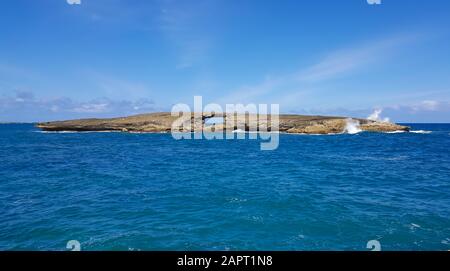 Eine Welle bricht auf der kleinen Insel vor der Küste von Oahu, Hawaii schießt Wasser hoch in die Luft. Stockfoto