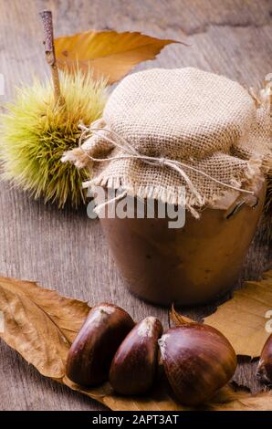 Auf dem rustikalen Tisch mit Herbstfarben, streichbarer Kastanienmarmelade, im Glasbecher Stockfoto