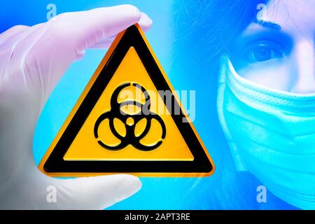 Hand, die ein Schild mit biologischer Gefährdung vor Mannequin mit Gesichtsmaske hält, Ausbruch eines Coronavirus Stockfoto