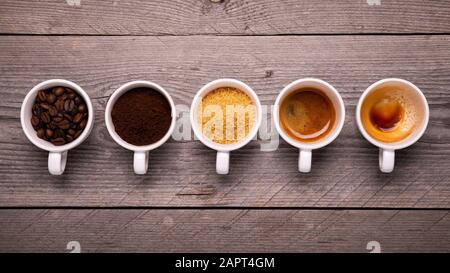 Draufsicht über eine Reihe von Tassen mit Kaffeebohnen und gemahlenem Kaffee, Zuckerrohr und exprimiert Stockfoto