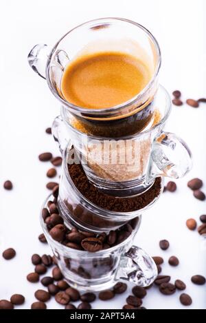 Glasbecher in vertikaler Reihenfolge, mit Kaffeebohnen, gemahlenem Kaffee, braunem Zucker und cremigem Getränk. Stillleben Stockfoto