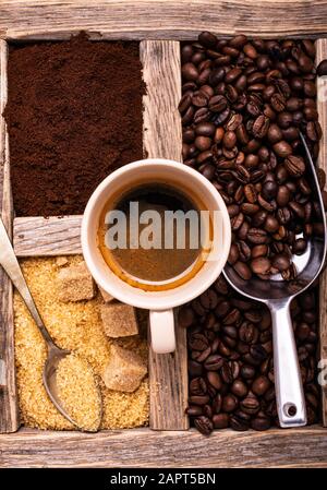 Im rustikalen Holzbehälter mit Draufsicht, einer Tasse Espresso, rohem Rohrzucker und geröstetem Kaffee. Stockfoto