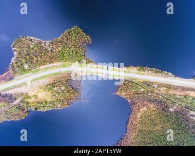 Schöner Blick von einer Straße durch den schönen See und Wald, auf beiden Seiten mit Wasser umgeben, oben von Drohne, luftige leuchtende Pic Stockfoto