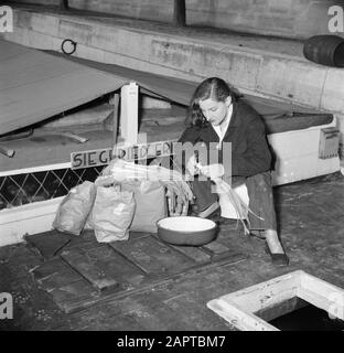 Das Segel-Hausboot Siegfried & Erik am Ufer der seine Auf dem Deck eines Schiffes Sitzend, schneidet eine Frau die Lauch; neben ihren Ständen Taschen mit Lebensmitteln Datum: 1950 Standort: Frankreich, Paris Schlüsselwörter: Lebensmittel, Gemüse, Schiffe, Frauen Stockfoto