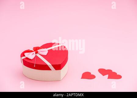 Herzförmige Geschenkbox und rote Papierherzen auf pinkfarbenem Pastellhintergrund. Valentines Tageskonzept Stockfoto