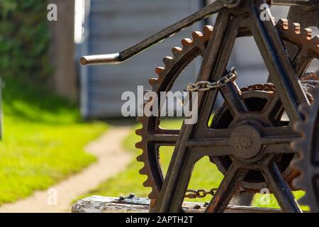 Eine mechanische Krabbenwinde, die von Hand an einer Schleusenstation an einem Kanal betrieben wird, ist an einem sonnigen Tag im Profil gegen Gras und einen Fußweg zu sehen. Stockfoto