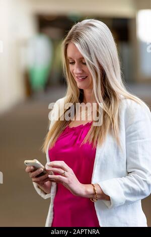 Eine professionelle reife Geschäftsfrau, die ihr Smartphone auf einem Flur auf Nachrichten überprüft; Edmonton, Alberta, Kanada Stockfoto