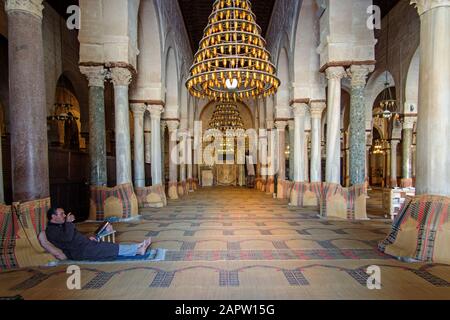 Ein Mann, der auf dem Boden bei der Kolonnade des Betzimmers Der Großen Moschee in Kairouan, Tunesien, liest Stockfoto