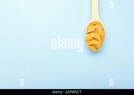 Flacher Holzlöffel mit cremiger Erdnussbutter mit Kopierraum auf blauem Hintergrund. Flat Lay mit Platz für Text für Erdnussbutter, Erdnuss Stockfoto