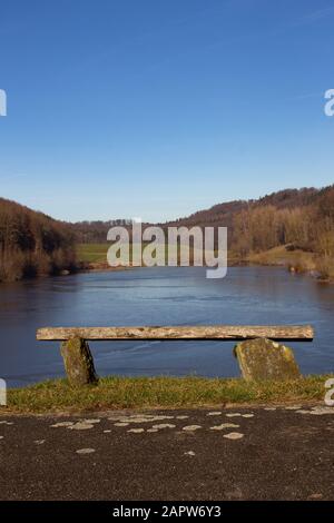 Auf einem Hügel mit Blick auf einen zugefrorenen See stand eine leere alte Holzbank Stockfoto