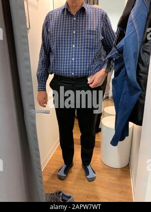 Vorderansicht des älteren Mannes im Kleiderladen Bestückungsraum mit neuen Hosen Stockfoto