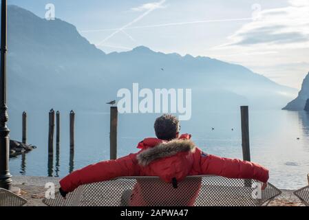 Der auf einer Bank entspannende Mann bewundert den Blick auf den Gardasee Stockfoto