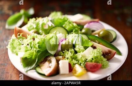 Gesunder Salat mit Fetakäse, grünen Oliven, Gurken, roter Zwiebel, grünem Pfeffer, verschiedenen Tomaten und frischem Basilikum. Nahaufnahme. Stockfoto