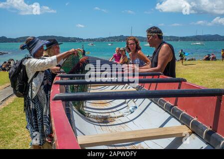 Ein Maori Kaumatua (Ältester), der sich an einen Waka (Maori Canoe) lehnt, spricht über die Webart seines Schals an eine Gruppe von Besuchern am Waitangi.Day in Waitangi. Stockfoto