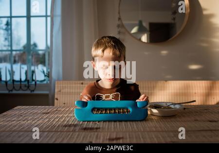 Junger Junge spielt in seinem iPad zu Hause beim Frühstück Stockfoto