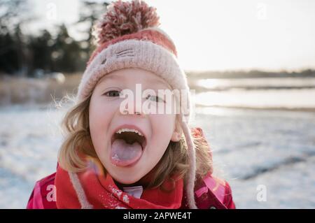 Junges Mädchen, das im Winter draußen Schnee auf der Zunge fängt Stockfoto