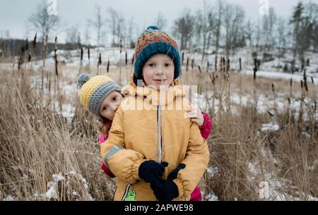 Bruder und Schwester spielen und schauen auf die Kamera, während sie draußen im Schnee sind Stockfoto