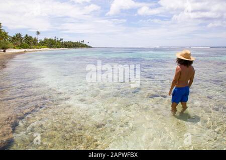 Mann mit lockigem Haar und goldenem Hut in felsigen Strand mit Palmen Stockfoto