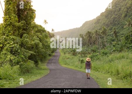 Mann mit Sonnenhut und lockigen Haaren, der auf einer leeren Straße in tropischer Gegend unterwegs ist Stockfoto