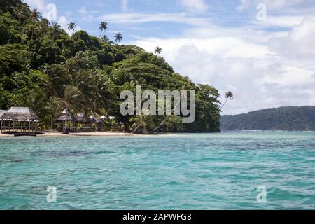 Strandbungalows und schiefe Palmen auf der tropischen Insel Samoa Stockfoto