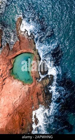 Luftaufnahme eines gefüllten Rockpools in der Nähe der Küste mit Wellen, die in die Tiefe stürzen Stockfoto