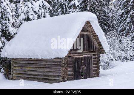 Holzbergschuppen vor dem Hintergrund verschneiten Bergen und Bäumen. Winteralpine Landschaft in Österreich. Schöner, natürlicher Hintergrund. Stockfoto