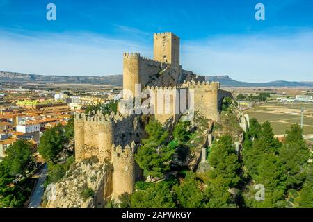 Luftaufnahme der mittelalterlichen Burg Almansa mit Donjon und Innenhof auf einem Felsen, der von dem von einem runden Ring aus roten Dachhäusern umgebenen Plateau auftaucht Stockfoto