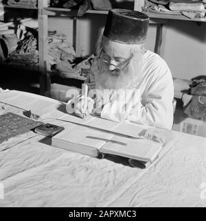 Israel 1964-1965: Jerusalem (Jerusalem), Thorarrolls Torah Writer at Work hinter einem Arbeitstisch Anmerkung: Die Tora (das Mosaische Gesetz) ist auf einer Rolle geschrieben, die aus Pergament von der Haut eines koscheren Tieres besteht. Die verschiedenen Teile von Pergament sind mit einer Sehne aneinander befestigt, der Text wird handschriftlich geschrieben. Die Tinte wird oft von selbst hergestellt und muss bestimmte Anforderungen erfüllen. Schließlich ist die Rolle an zwei Holzstöcken mit Griffen befestigt und beide Enden werden gegen das mittlere Datum gerollt: 1964 Ort: Israel, Jerusalem Schlüsselwörter: Tora, Handschrift, jüdische Religion, Schriftsteller, Arbeit Stockfoto