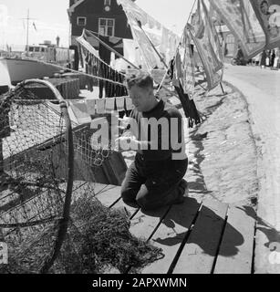 Volendam Fischer in Volendam beschäftigt sich mit der Reparatur der Netze, hinter ihm hängt die Wäsche Datum: 1. September 1959 Ort: Noord-Holland, Volendam Schlüsselwörter: Fischernetze, Fischer, Fischereifahrzeuge, Wäsche Stockfoto