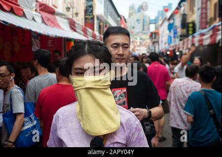 24.01.2020, Singapur, Republik Singapur, Asien - EINE Frau bedeckt ihr Gesicht mit einer Maske auf einem Straßenbasar in Chinatown. Stockfoto