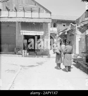 Israel 1964-1965: Jerusalem (Jerusalem), Mea Shearim Shop im Bezirk Mea Shearim, ein Passant trägt ein Sitzkissen in der Öffentlichkeit (vermutlich wegen Sauberkeit) Anmerkung: MEA Shearim, auch Meah Shearim oder hundert Tore genannt, ist einer der ältesten Bezirke Jerusalems. Sie wurde ab etwa 1870 von hasidischen Juden erbaut, die bis dahin in der Altstadt lebten. Es war jedoch zu wenig Platz und so kauften sie ein Stück Land nordwestlich der Stadt. Dieses Land, ein Sumpfgebiet, wurde zu Land kultiviert, um ein neues Stadtviertel zu errichten: Meah Shearim. Der Bezirk ist anno 2012 als der größte bekannt Stockfoto