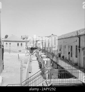 Israel 1964-1965: Jerusalem (Jerusalem), Mea Shearim Wohnhäuser auf einer Galerie, eine Reihe von Bewohnern, die außerhalb in der Türöffnung stehen Anmerkung: MEA Shearim, auch Meah Shearim oder hundert Tore genannt, ist einer der ältesten Bezirke Jerusalems. Sie wurde ab etwa 1870 von hasidischen Juden erbaut, die bis dahin in der Altstadt lebten. Es war jedoch zu wenig Platz und so kauften sie ein Stück Land nordwestlich der Stadt. Dieses Land, ein Sumpfgebiet, wurde zu Land kultiviert, um ein neues Stadtviertel zu errichten: Meah Shearim. Der Distrikt ist anno 2012 als das extremste orthodoxe Juwis bekannt Stockfoto