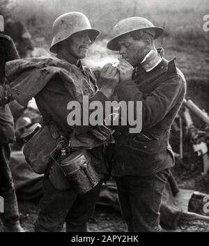 Ein deutscher Kriegsgefangener gibt einem verwundeten englischen Soldaten, einem Tommy, ein Feuer zur Beleuchtung einer Zigarette während des Ersten Weltkriegs, Ort und Jahr unbekannt. Stockfoto