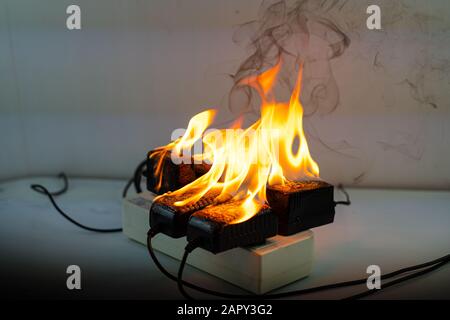 Bei einem Feueradapterladegerät an der Steckdosenleiste auf schwarzem Hintergrund ist ein elektrischer Kurzschluss aufgetreten, der zu einer Verbrennung des Stromkabels führt Stockfoto