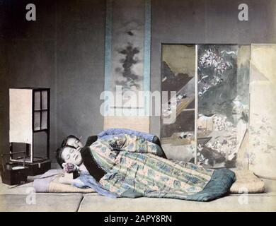 Schlafen in Japan. Zwei Frauen schlafen unter einer gesteppten Decke in einem Raum mit bemaltem Raumschirm, Wandrolle (Papierbemalung) und einer Papierlaterne als Nachtlicht. Ihr Kopf ruht auf einem japanischen Kissen. Diese besteht aus einem etwa zehn bis dreizehn Zentimeter hohen Holzkiste. Auf der Kiste befindet sich ein kleines Kissen. Oft wird dies mit Papierrollen als Kissenbezug geliefert. Die Kiste kann auch als "toilettenbeutel" dienen. Undatiert [um 1880-1890], Ort unbekannt. Handfarbiges Albumin. [Foto, das zu einer Serie von 42 Drucken in der Sammlung von Spaarnestad Photo von Felice Beato, Kusakabe Kimbei oder von Raimund gehört Stockfoto