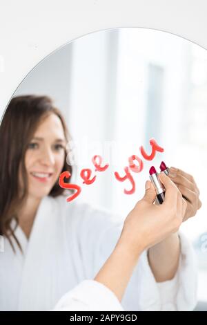 Hand der fröhlichen jungen Brunette-Frau in weissem weichen bademantel mit Lippenstift Stockfoto