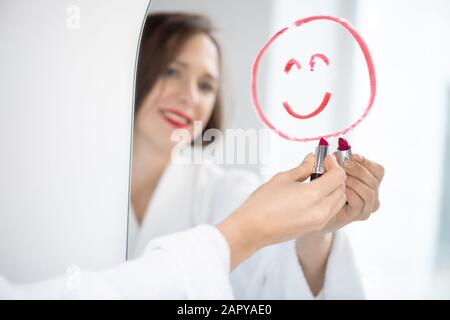Hand der hübschen jungen fröhlichen Frau im bademantel, die mit einem Lächeln ins Gesicht zieht Stockfoto