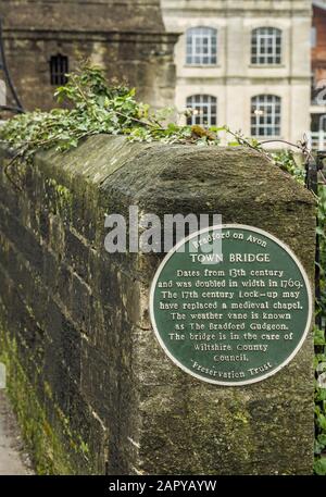 Eine erklärende runde grüne Plakette auf dem berühmten Bradford an der Avon Brücke über den Fluss Avon in West Wiltshire, England. Dahinter steht das alte Gefängnis. Stockfoto